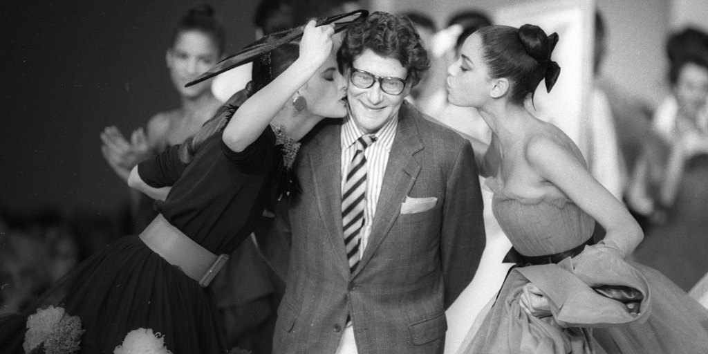 French designer Yves Saint Laurent is kissed by models at the end of his fashion show in Paris October 21, 1987. REUTERS/Luc Novovitch (FRANCE)  BEST QUALITY AVAILABLE - RTR21B68